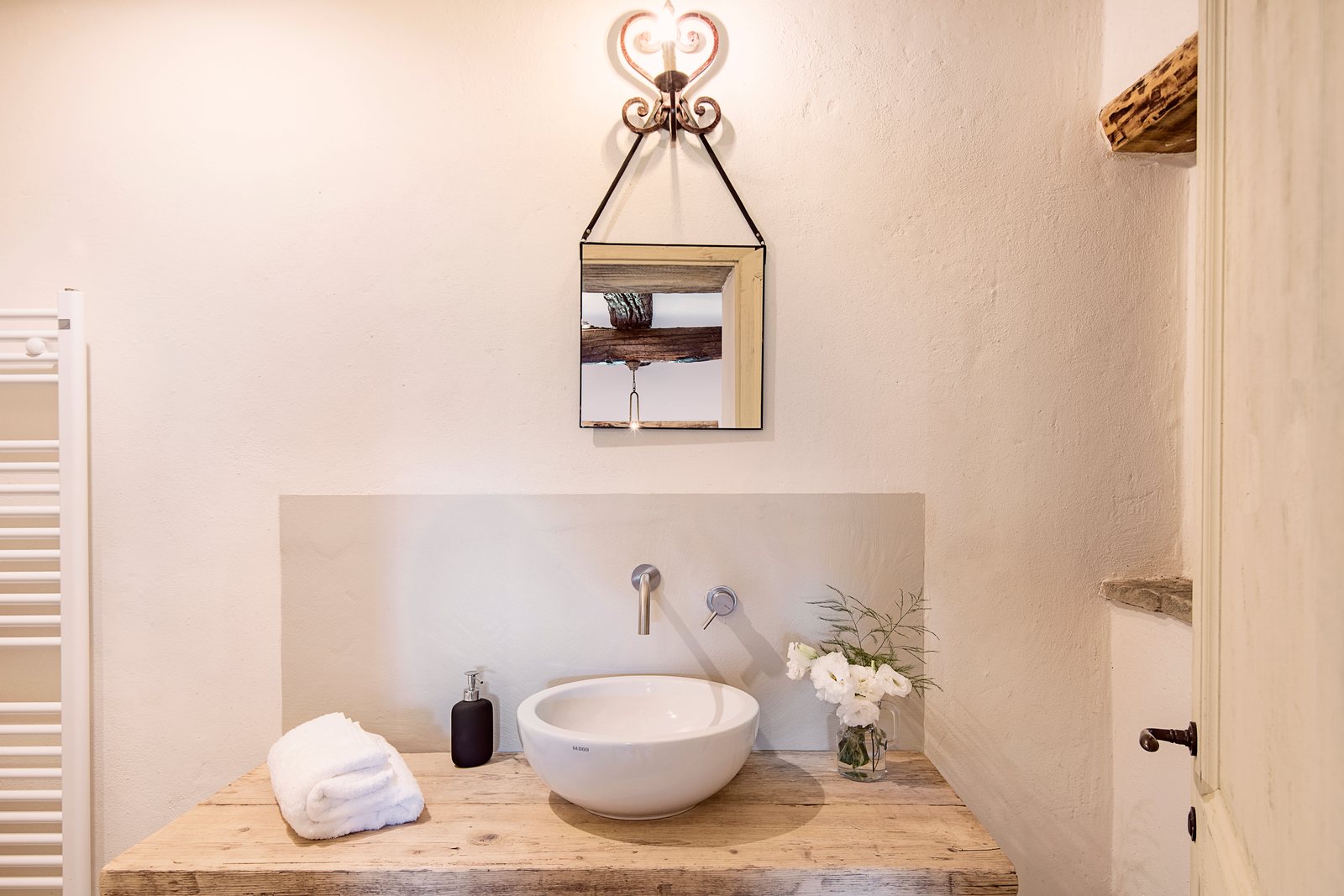Bathroom with a white vessel sink on a wooden top and an iron wall lamp
