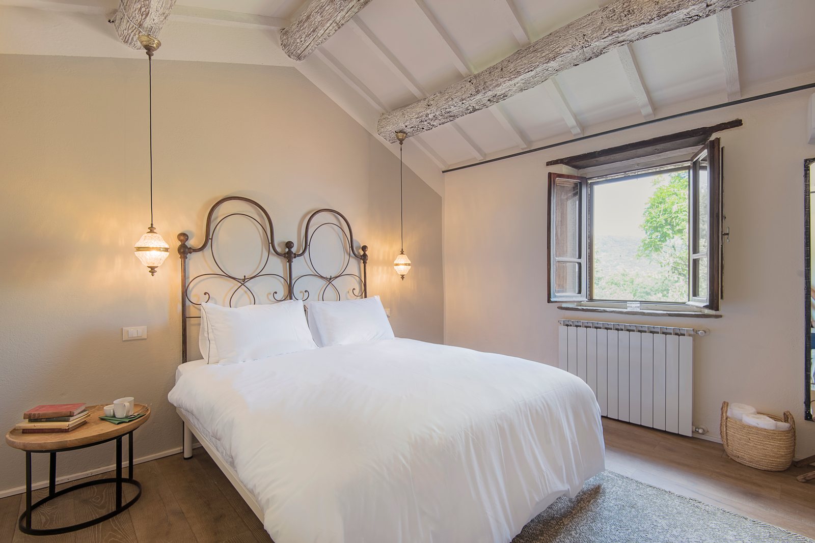 Double bedroom with a wrought iron bed, white linen and a window onto the trees