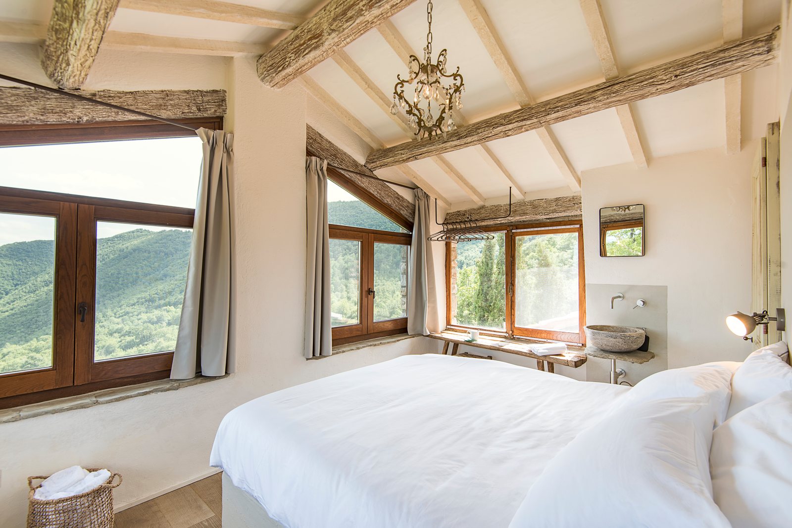 Bright double bedroom under wooden beams, with windows onto the hills