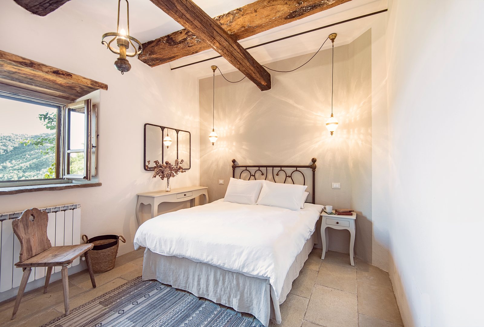 Double bedroom with an iron bed, oak beams, glass pendant lamps and a window onto the hills