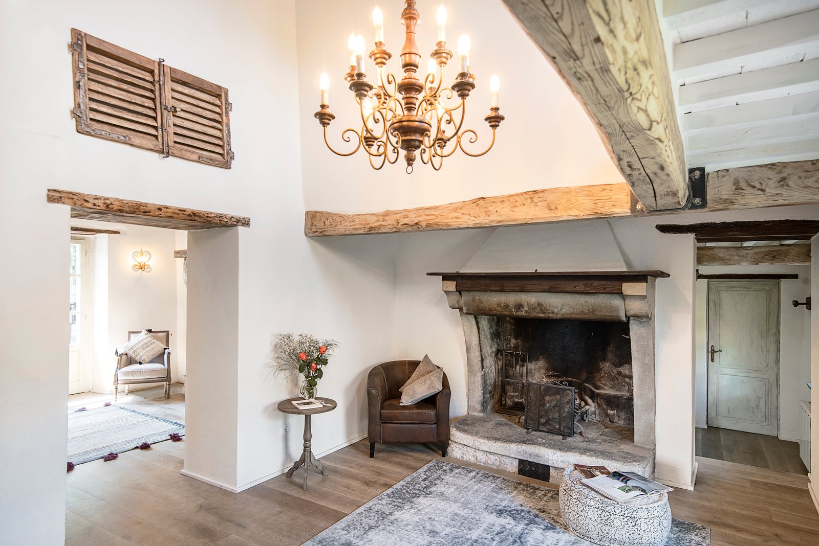 Double-height room with an iron chandelier, a stone fireplace and old oak beams
