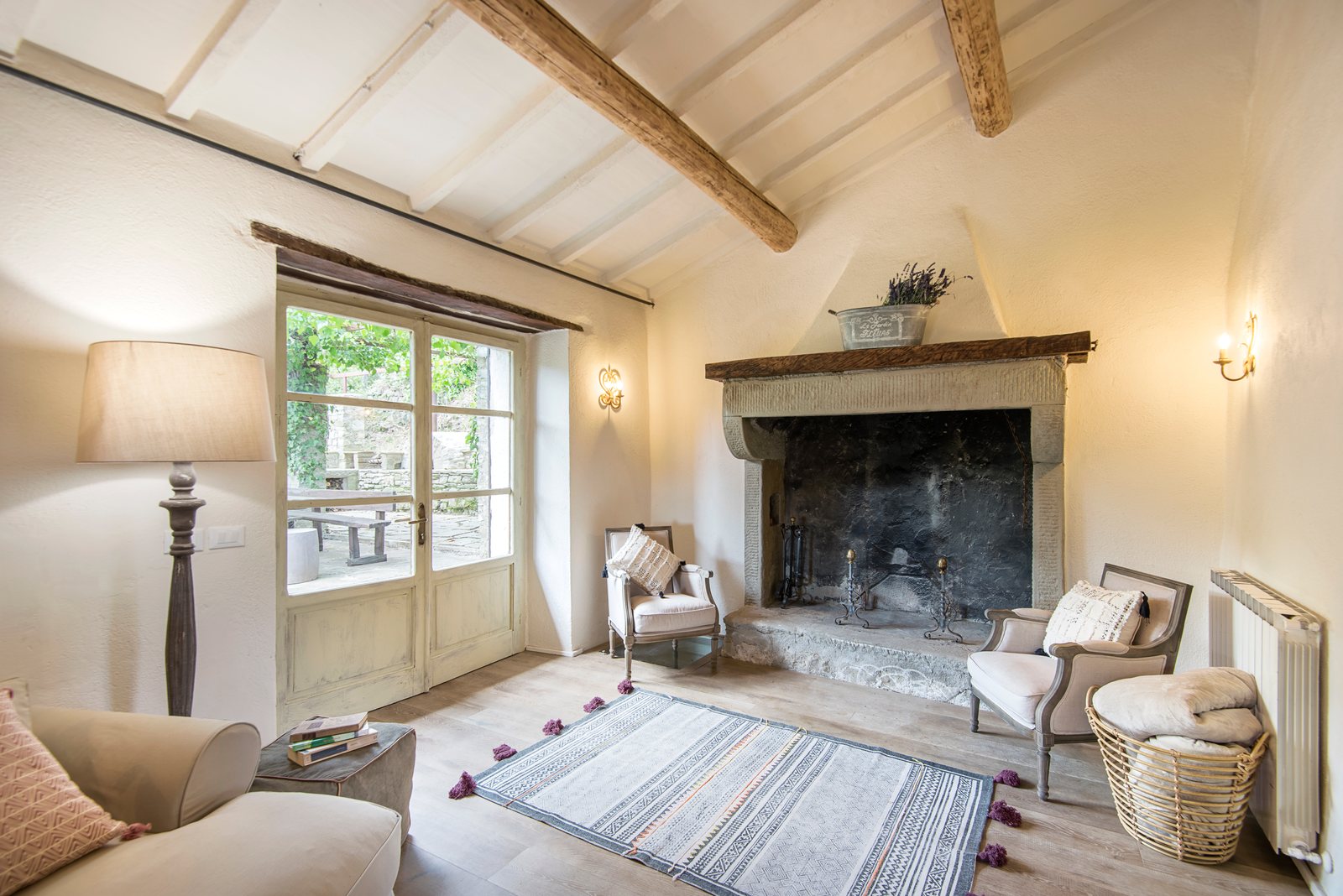 Living room with a large stone fireplace, beamed ceiling and armchairs