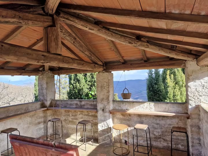 The tower bar: a covered stone terrace under a timber roof, with bar stools along a ledge and a view over the valley